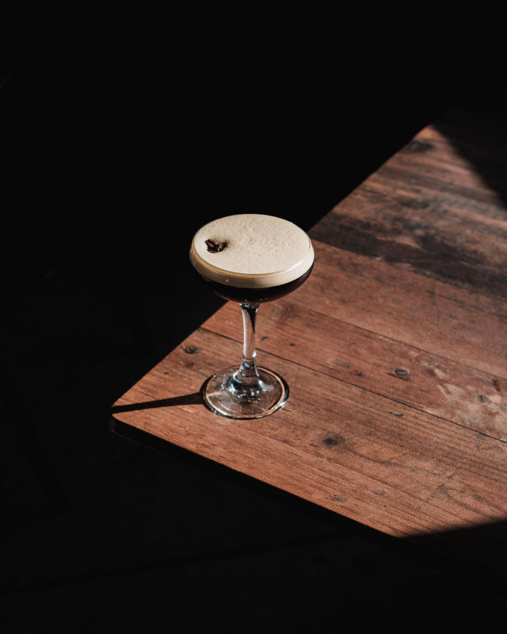 Dark espresso martini cocktail with foam on wooden surface