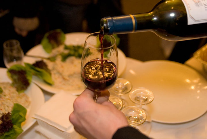 Close-up shot of red wine being poured into a glass at dinner