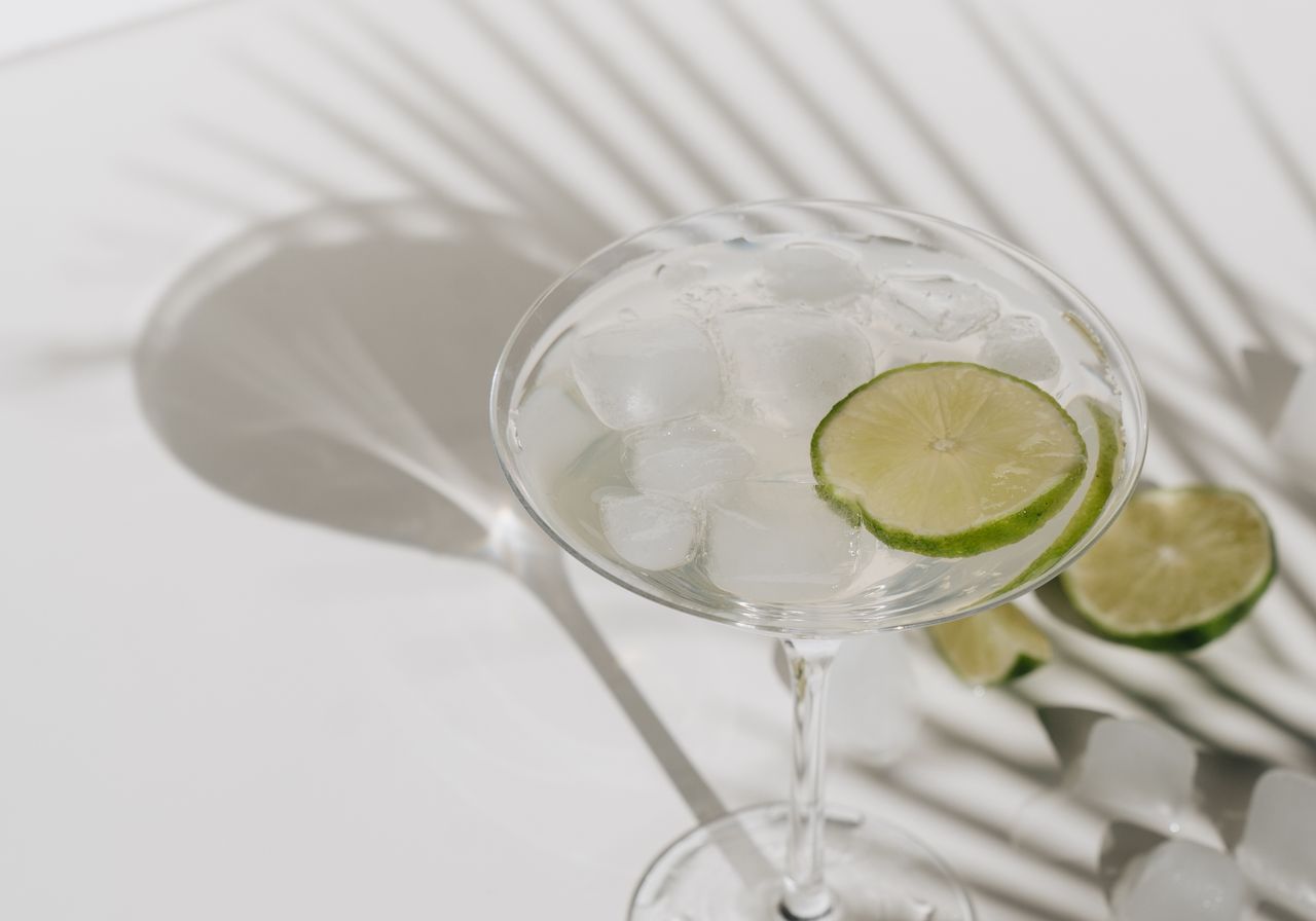 Chilled lime margarita with ice on a bright table with palm-leaf shadows